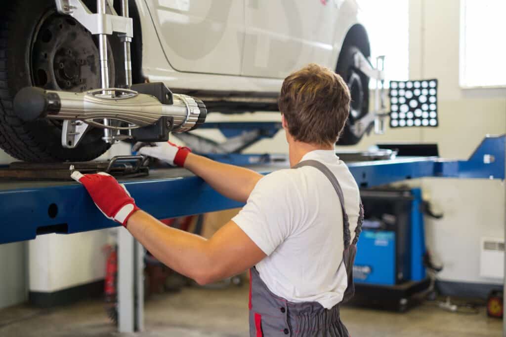 Young serviceman checking wheel alignment  in a car workshop. Tire Rotation and Wheel Alignment