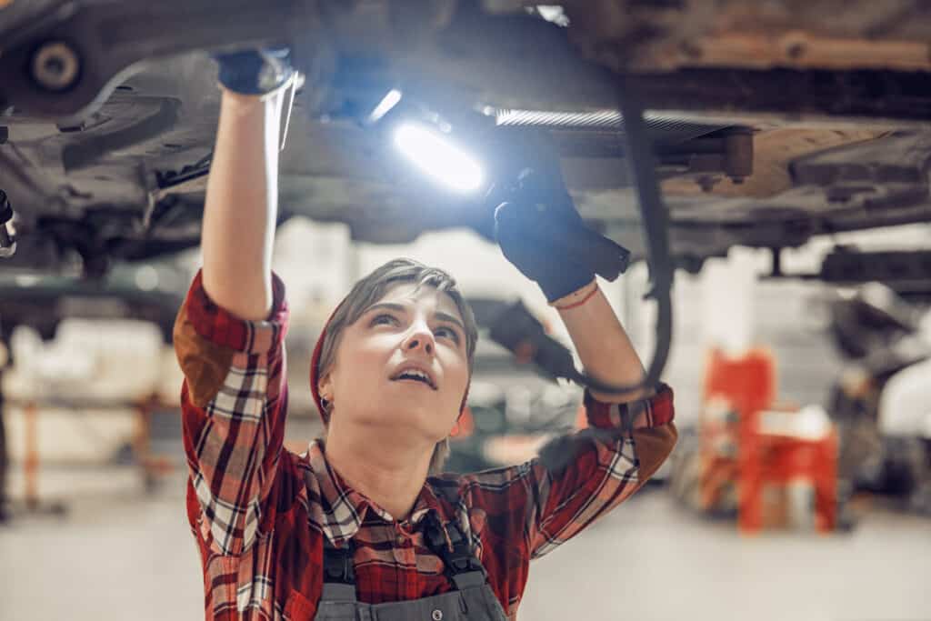Female technician working with a flashlight under a lifted car. The Outlook of Mechanics with the Rise of Electric Cars